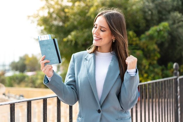 Young pretty woman holding a passport at outdoors celebrating a victory