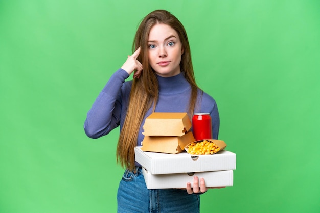 Young pretty woman holding pizzas and burgers over isolated chroma key background thinking an idea