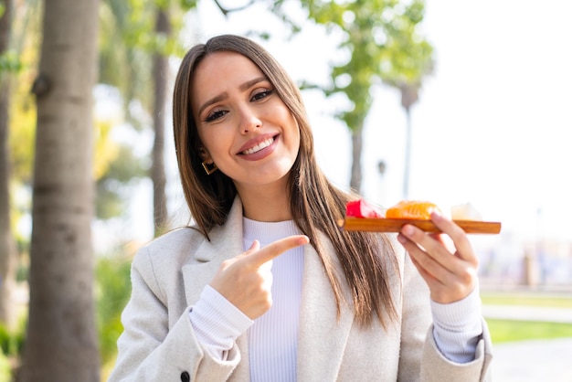 屋外で刺身を保持し、それを指している若いきれいな女性