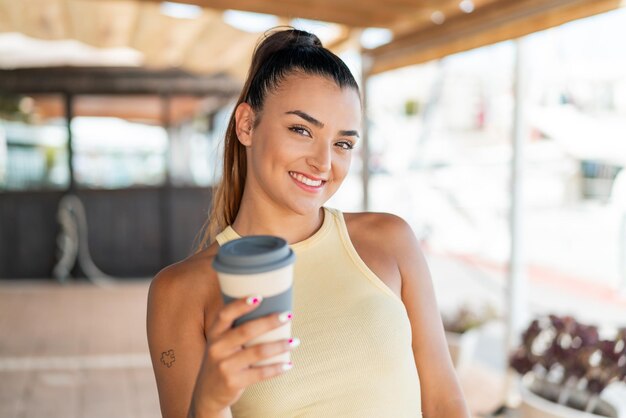 屋外で幸せな表情でコーヒーをテイクアウトする若いきれいな女性