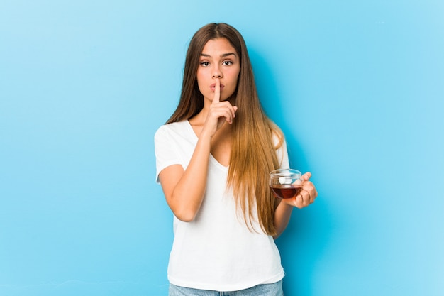 Young pretty woman holding a tea cup keeping a secret or asking for silence.