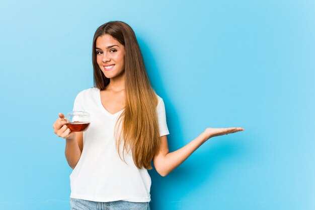 Young pretty woman holding a tea cup showing a on a palm and holding another hand on waist.