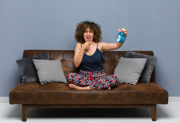 Young pretty woman at home sitting on a sofa with a clock