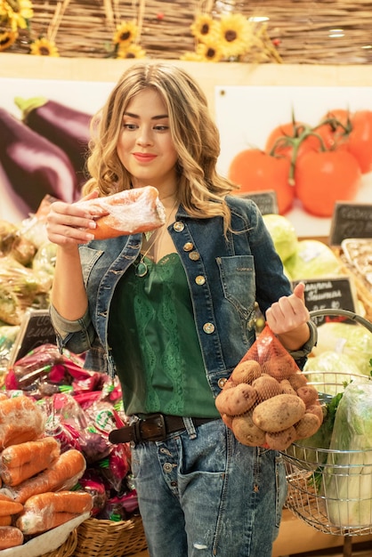 若いきれいな女性はスーパーマーケットで野菜を買うことを選んでいます