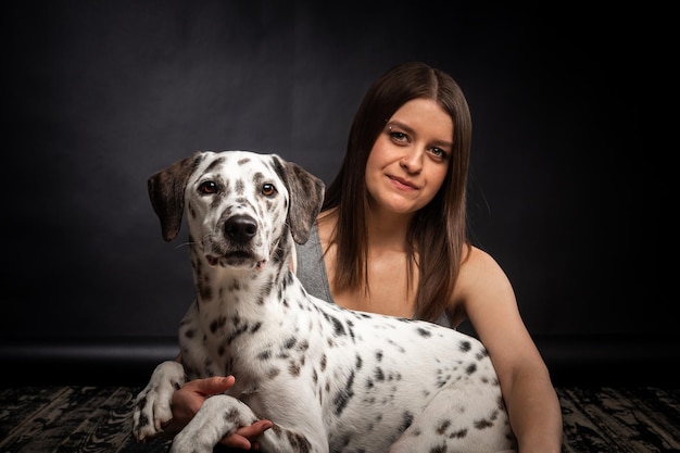 A young pretty woman is playing with her Dalmatian pet isolated on a black background