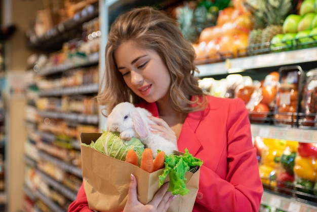 若いきれいな女性はスーパーマーケットで彼女のペットの白いウサギのために野菜を買うために買い物をしています