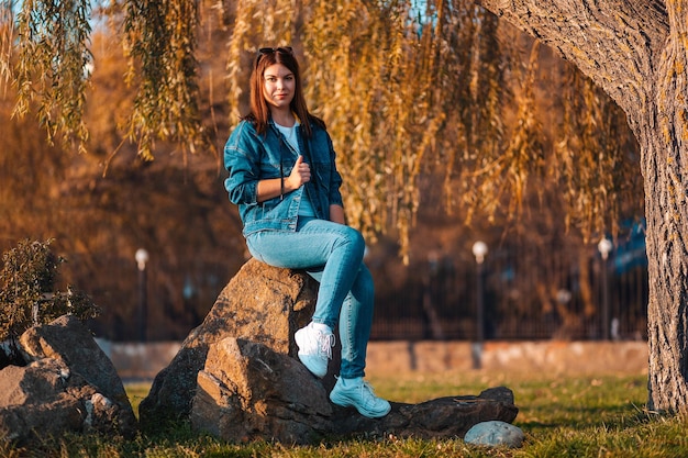 A young pretty woman is sitting on a rocks in an autumn park The concept of psychology