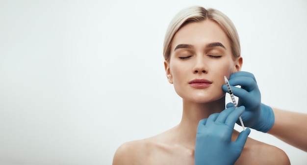 Young pretty woman keeping her eyes closed while doctors hand making an injection in her