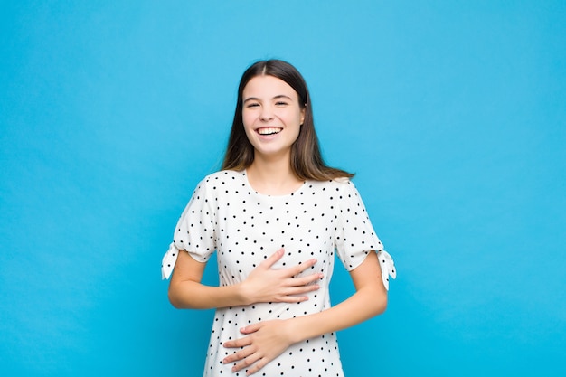 Giovane bella donna ridere ad alta voce per uno scherzo divertente, sentirsi felice e allegro, divertirsi contro il muro blu