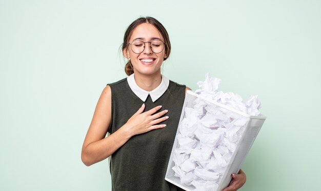 いくつかの陽気な冗談で大声で笑っている若いきれいな女性。紙球ゴミ箱の概念