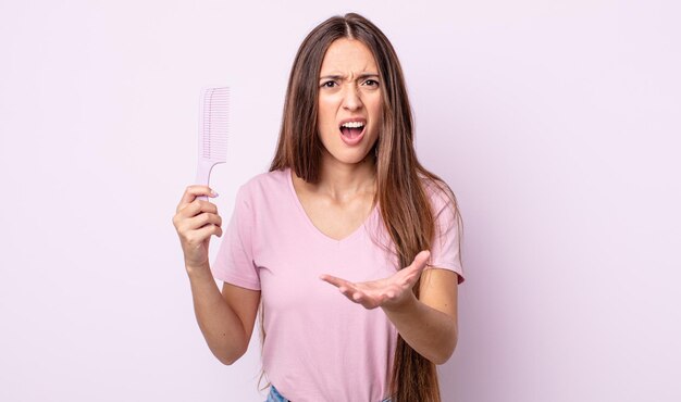 Giovane donna graziosa che sembra arrabbiata, infastidita e frustrata. concetto di pettine per capelli