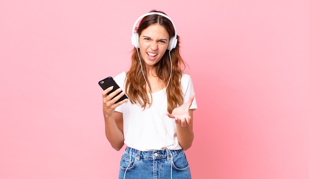 Young pretty woman looking angry, annoyed and frustrated with headphones and a smartphone