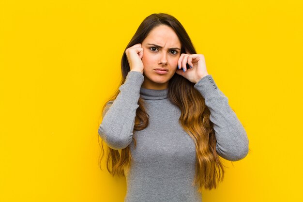 Young pretty woman looking angry, stressed and annoyed, covering both ears to a deafening noise, sound or loud music job or business concept