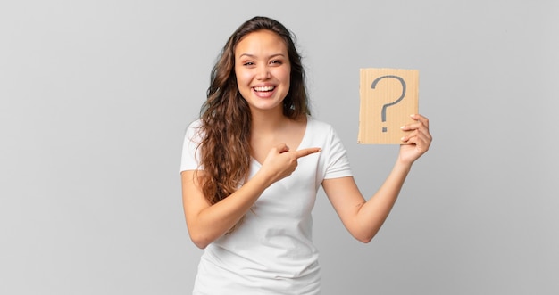 Young pretty woman looking excited and surprised pointing to the side and holding a question mark sign