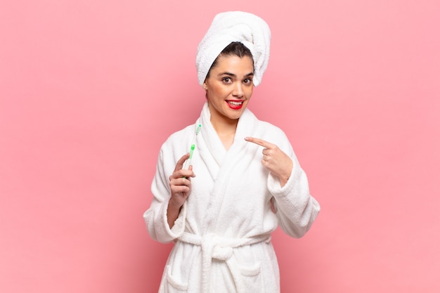 Young pretty woman looking excited and surprised pointing to the side and upwards to copy space. bathrobe and toothbrush concept