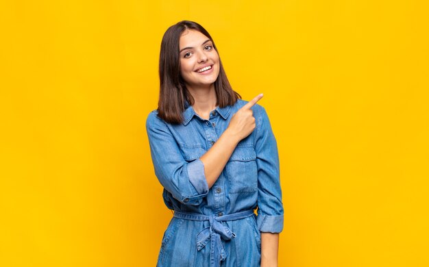 Giovane donna graziosa che sembra eccitata e sorpresa che punta di lato e verso l'alto per copiare lo spazio