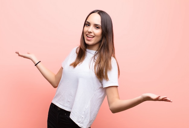 Young pretty woman looking happy, arrogant, proud and self satisfied, feeling like a number one against pink wall