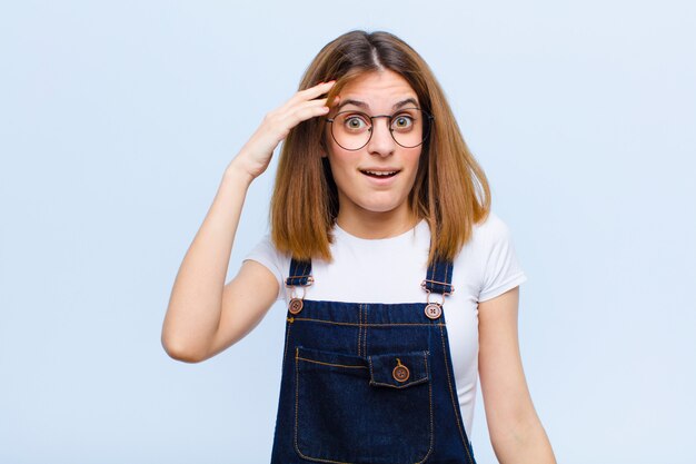 Young pretty woman looking happy, astonished and surprised, smiling and realizing amazing and incredible good news against blue wall