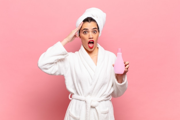 Young pretty woman looking happy, astonished and surprised, smiling and realizing amazing and incredible good news. bathrobe and face cleaning concept