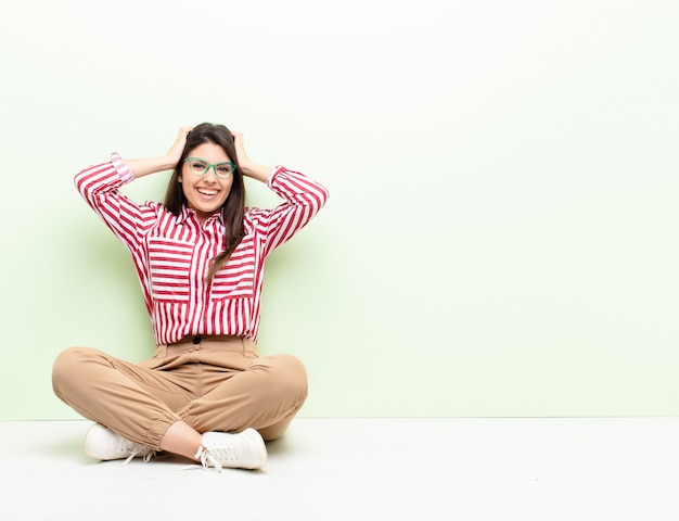 Young pretty woman looking happy, carefree, friendly and relaxed enjoying life and success, with a positive attitude sitting on the floor