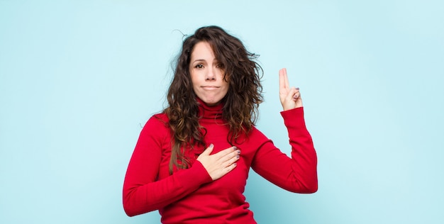 Young pretty woman looking happy, confident and trustworthy, smiling and showing victory sign, with a positive attitude against blue wall