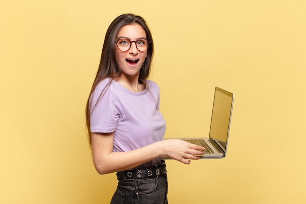 Young pretty woman looking happy and pleasantly surprised, excited with a fascinated and shocked expression. laptop concept