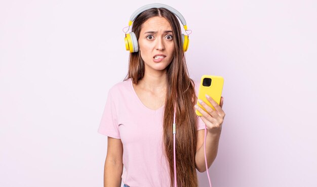 Young pretty woman looking puzzled and confused. headphones and smartphone