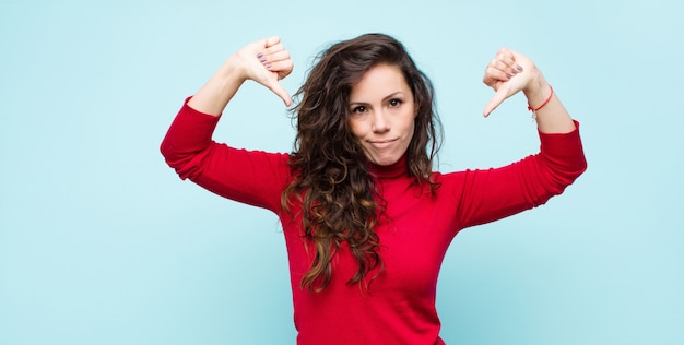 Photo young pretty woman looking sad, disappointed or angry, showing thumbs down in disagreement, feeling frustrated against blue wall