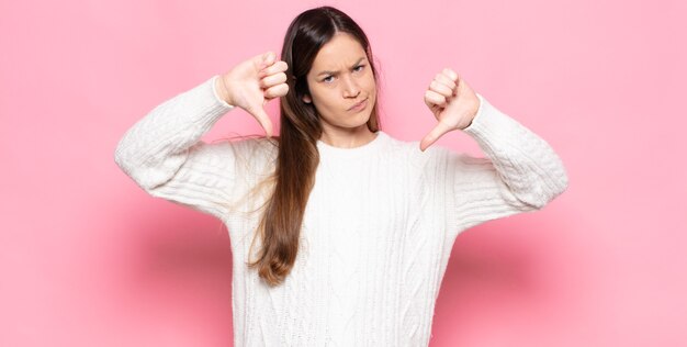 写真 悲しみ、失望、または怒りを見て、不一致で親指を下に見せ、欲求不満を感じている若いきれいな女性