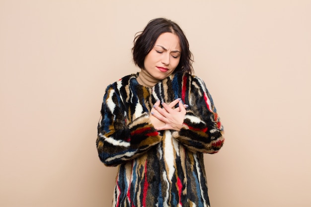 Photo young pretty woman looking sad, hurt and heartbroken, holding both hands close to heart, crying and feeling depressed against beige wall