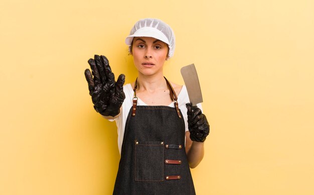 Young pretty woman looking serious showing open palm making stop gesture butcher concept