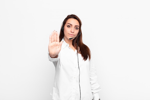 Young pretty woman looking serious, stern, displeased and angry showing open palm making stop gesture with headphones and microphone