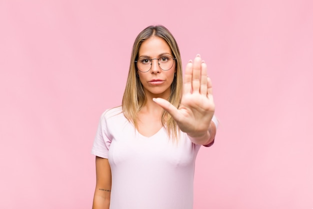 Young pretty woman looking serious, stern, displeased and angry showing open palm making stop gesture