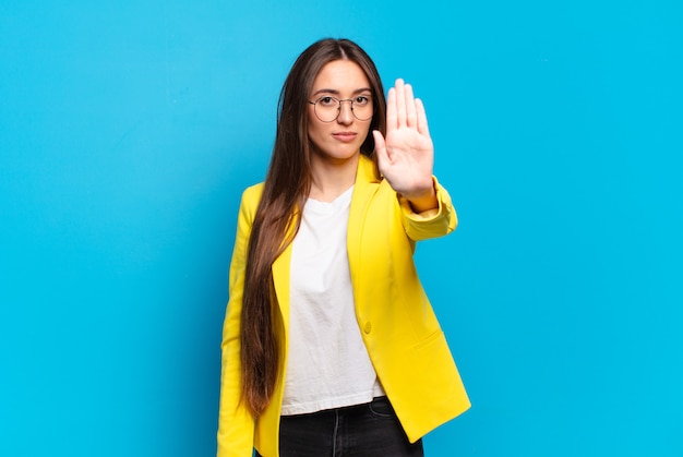 Young pretty woman looking serious, stern, displeased and angry showing open palm making stop gesture