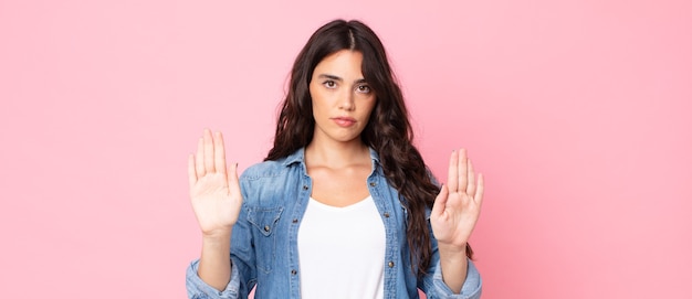 Foto giovane bella donna che sembra seria, infelice, arrabbiata e dispiaciuta che vieta l'ingresso o dice stop con entrambi i palmi aperti