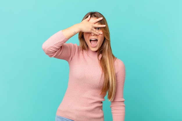 Young pretty woman looking shocked, scared or terrified, covering face with hand