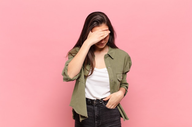 Young pretty woman looking stressed, ashamed or upset, with a headache, covering face with hand