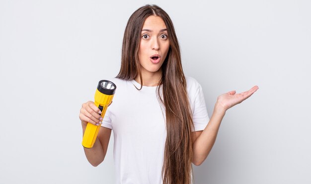 Young pretty woman looking surprised and shocked, with jaw dropped holding an object. lantern concept