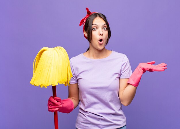 Young pretty woman looking surprised and shocked, with jaw dropped holding an object with an open hand on the side