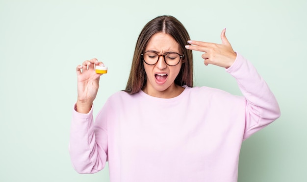 Young pretty woman looking unhappy and stressed, suicide gesture making gun sign. contact lenses concept