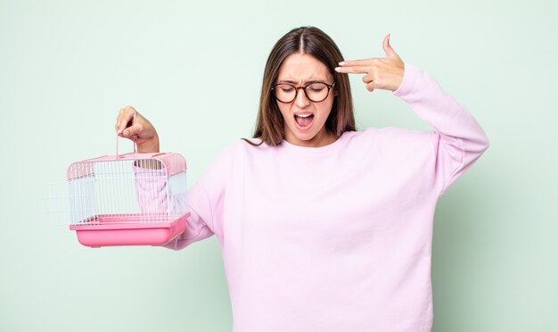 young pretty woman looking unhappy and stressed, suicide gesture making gun sign. pet cage concept