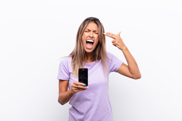 Young pretty woman looking unhappy and stressed, suicide gesture making gun sign with hand, pointing to head holding a smart telephone