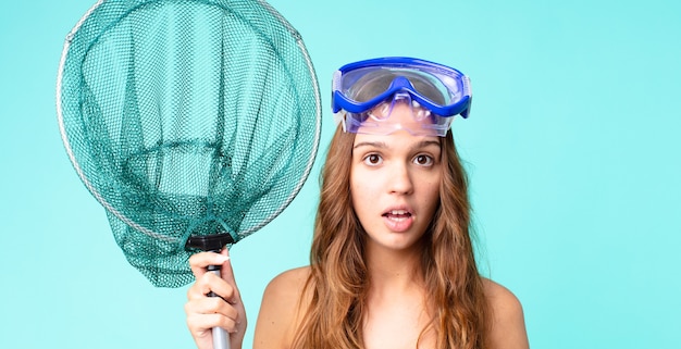 young pretty woman looking very shocked or surprised with goggles and a fishing net