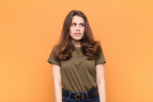 Young pretty woman looking worried, stressed, anxious and scared, panicking and clenching teeth against orange wall