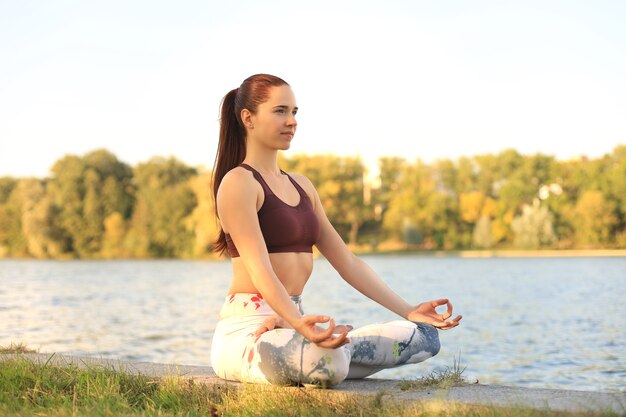 Young pretty woman in lotus pose in green park.