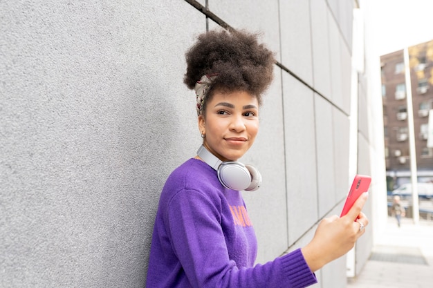 Photo young pretty woman, mixed race afro, on the street with headphones and smartphone happy smiling,