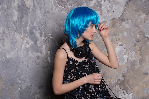 写真 若いきれいな女性または髪の毛のかつらの青い色のセクシーな女の子と灰色の壁のテクスチャ背景に音楽ヘッドセットまたはヘッドフォンのかわいい顔
