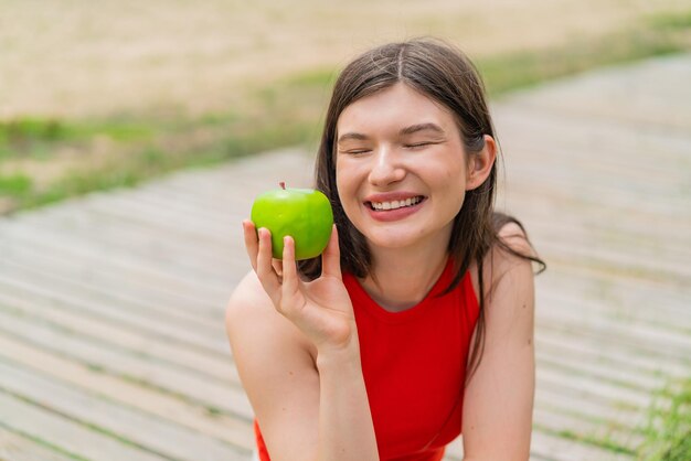 Photo young pretty woman at outdoors holding an apple with happy expression