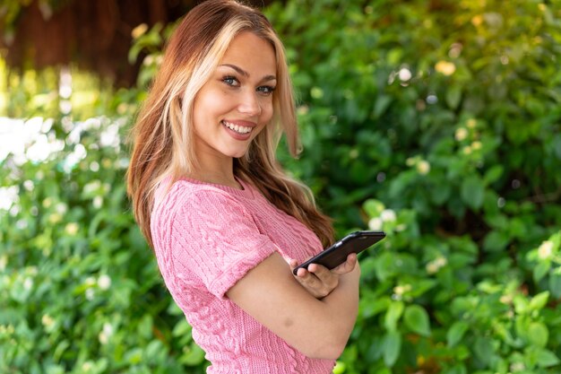 Young pretty woman at outdoors holding a mobile phone and with arms crossed