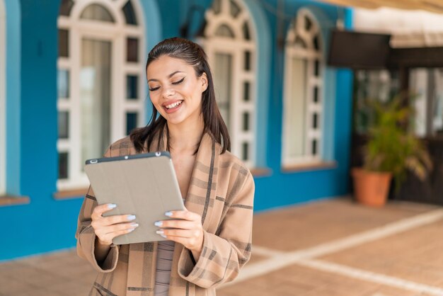 Young pretty woman at outdoors holding a tablet with happy expression